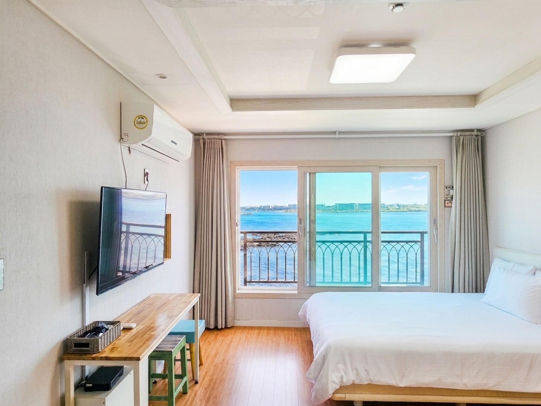 Habitación de hotel con cama, televisión, escritorio, ventana con vista al mar y balcón.