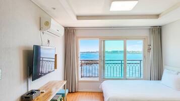 Habitación de hotel con cama, televisión, escritorio, ventana con vista al mar y balcón.