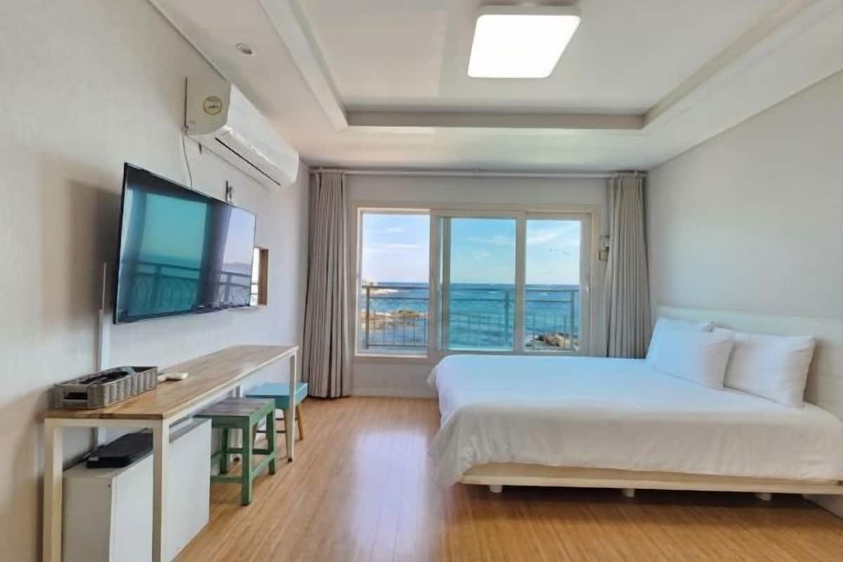 Habitación de hotel con cama, escritorio, televisor y ventana con vista al mar.
