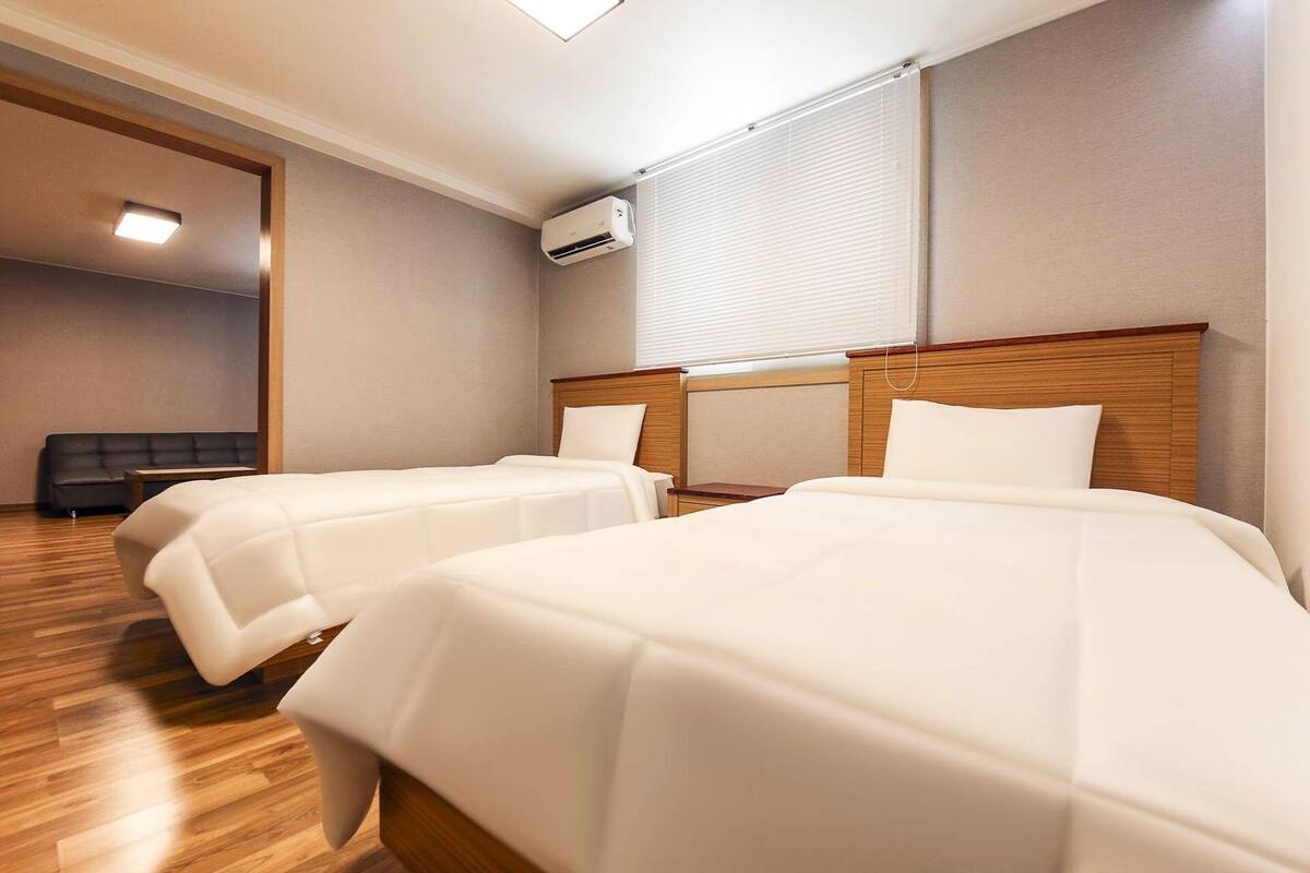 Une chambre d’hôtel avec deux lits, un canapé, un appareil de climatisation et un luminaire au plafond.