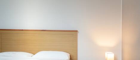 A neatly made bed with white linens, a wooden headboard, and a bedside table with a lamp.
