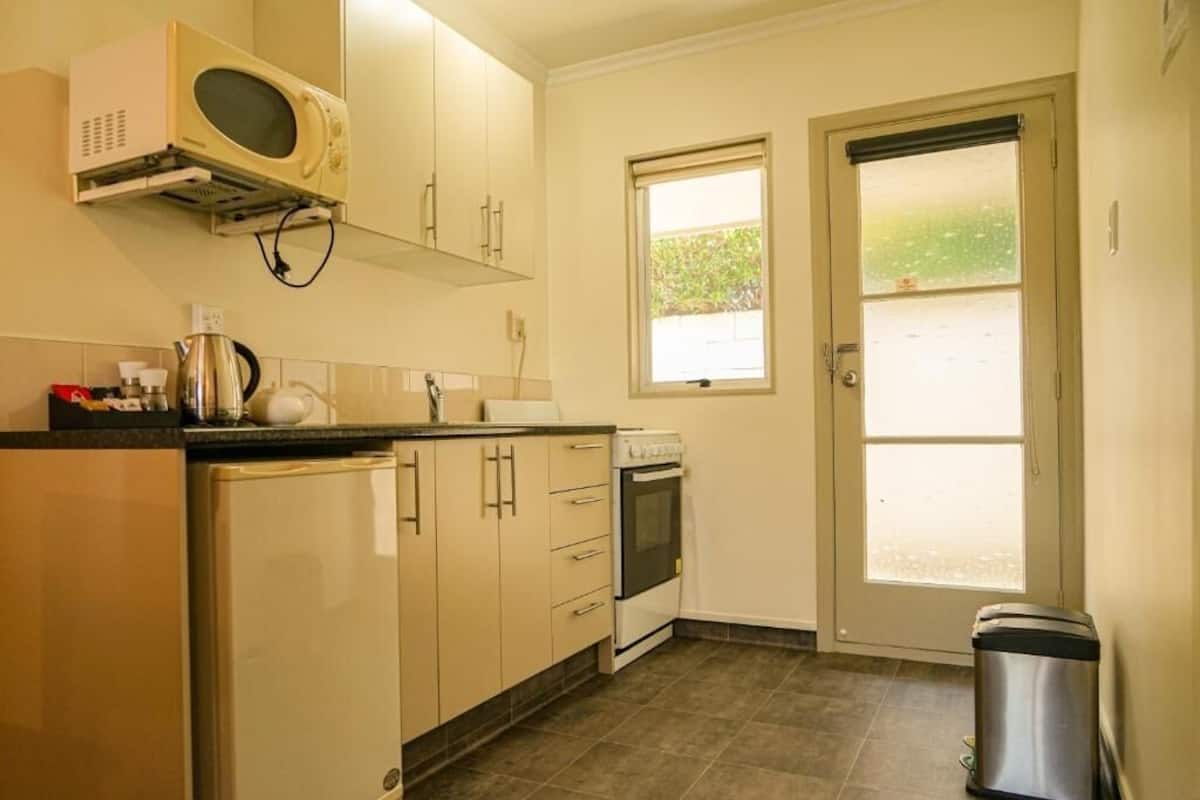 Une cuisine compacte équipée d’un four à micro-ondes, d’une cuisinière et d’un évier, avec une petite fenêtre et une porte donnant sur l’extérieur.