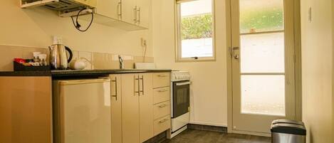 A compact kitchen with a microwave, stove, and sink, a small window, and a door leading outside.