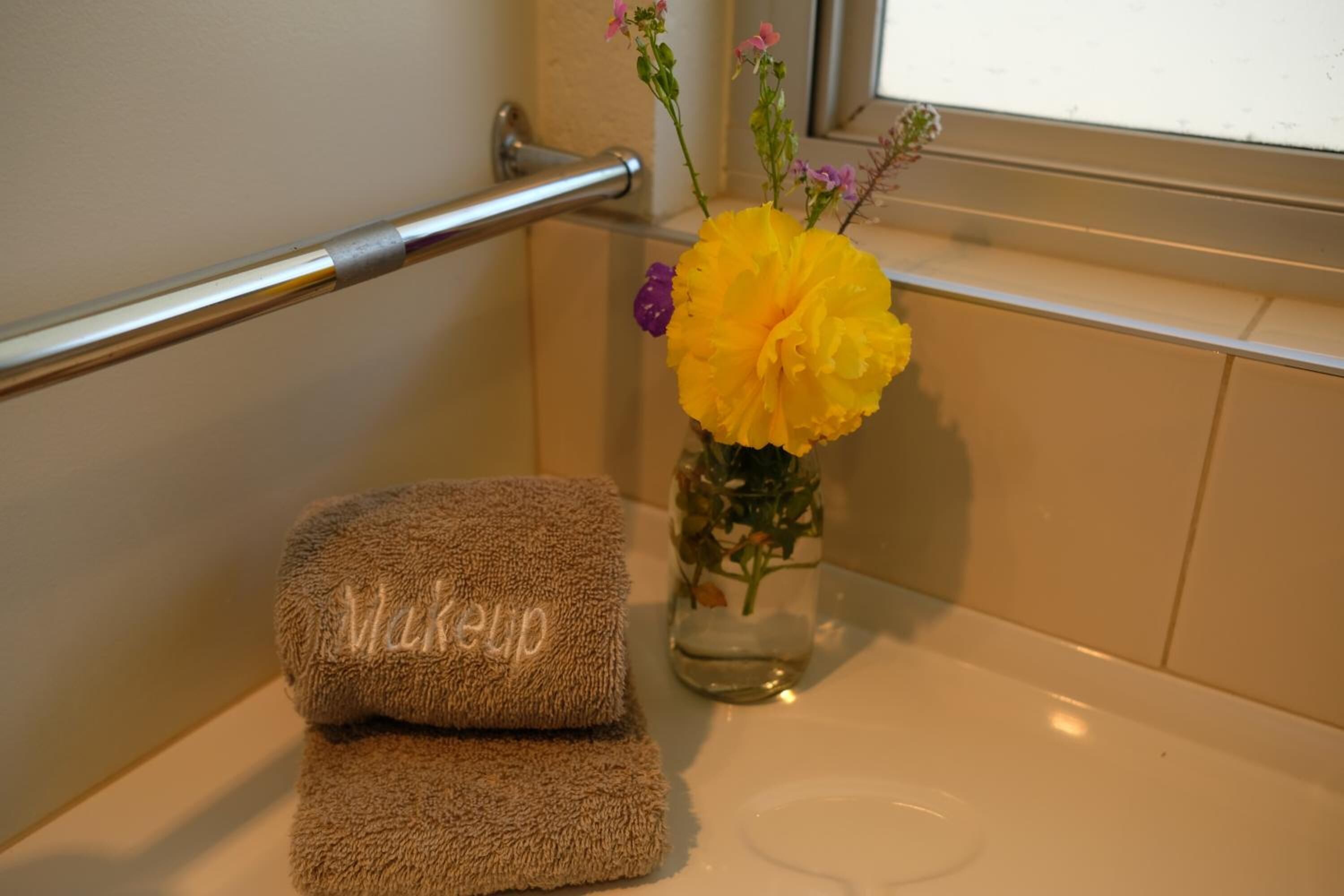 A bathroom with a towel rack, a glass vase with flowers, and a towel with the word "Makeup" on it.