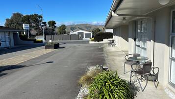 A motel with a paved driveway, outdoor seating, and a view of distant hills.