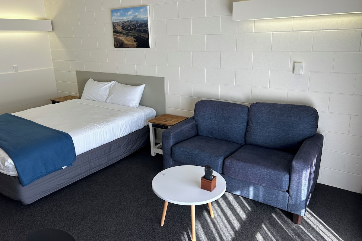 Une pièce comprenant un lit, un canapé, une petite table et un tableau au mur.