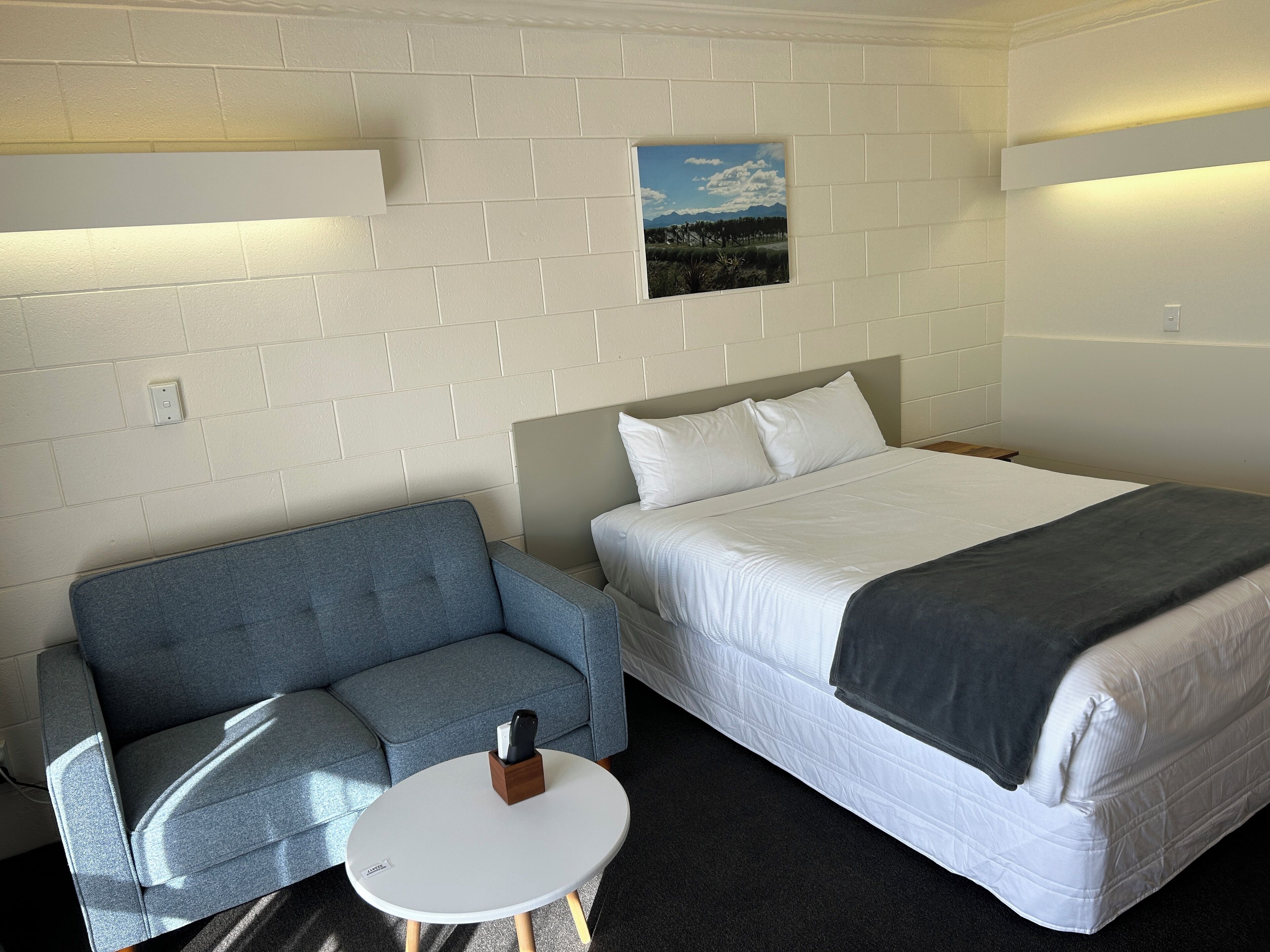 Ein Hotelzimmer mit einem Bett, einem grauen Sofa, einem kleinen runden Tisch und einem Bild an der Wand.