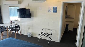 A room with a bed, a desk with chairs, a TV mounted on the wall, and a fire action notice.