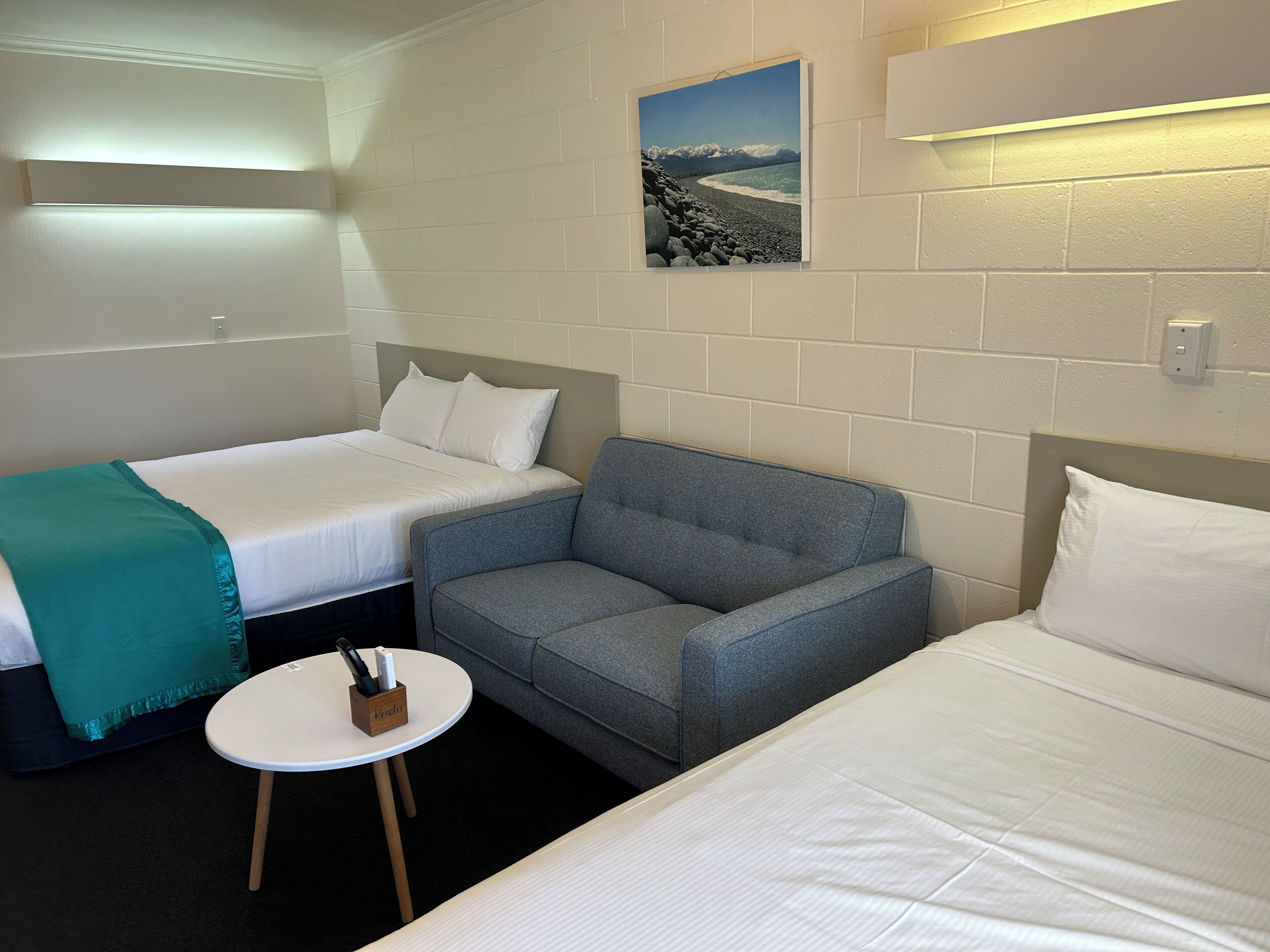 A hotel room with two beds, a gray sofa, a small table with a knife block, and a framed picture on the wall.