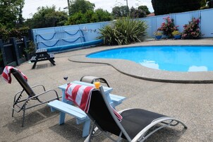 Un área junto a la piscina con dos sillones reclinables, una mesa de picnic y una mesa pequeña con una bebida.