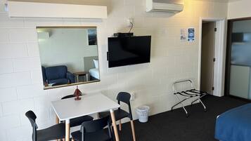 A compact hotel room with a single bed, a small table with chairs, a TV mounted on the wall, and a mirror reflecting the room.
