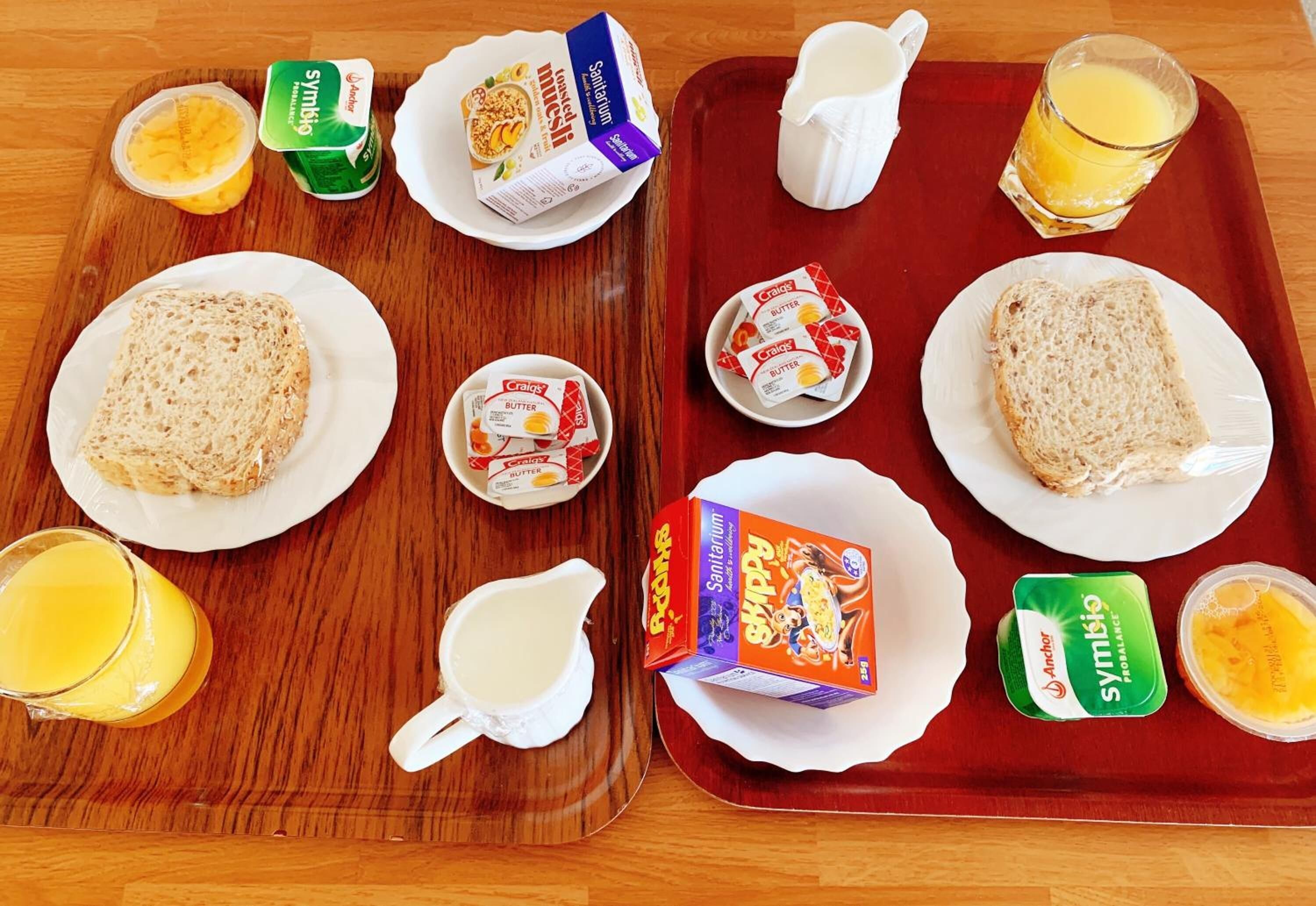 A breakfast tray with toast, butter, jam, orange juice, and a carton of milk.