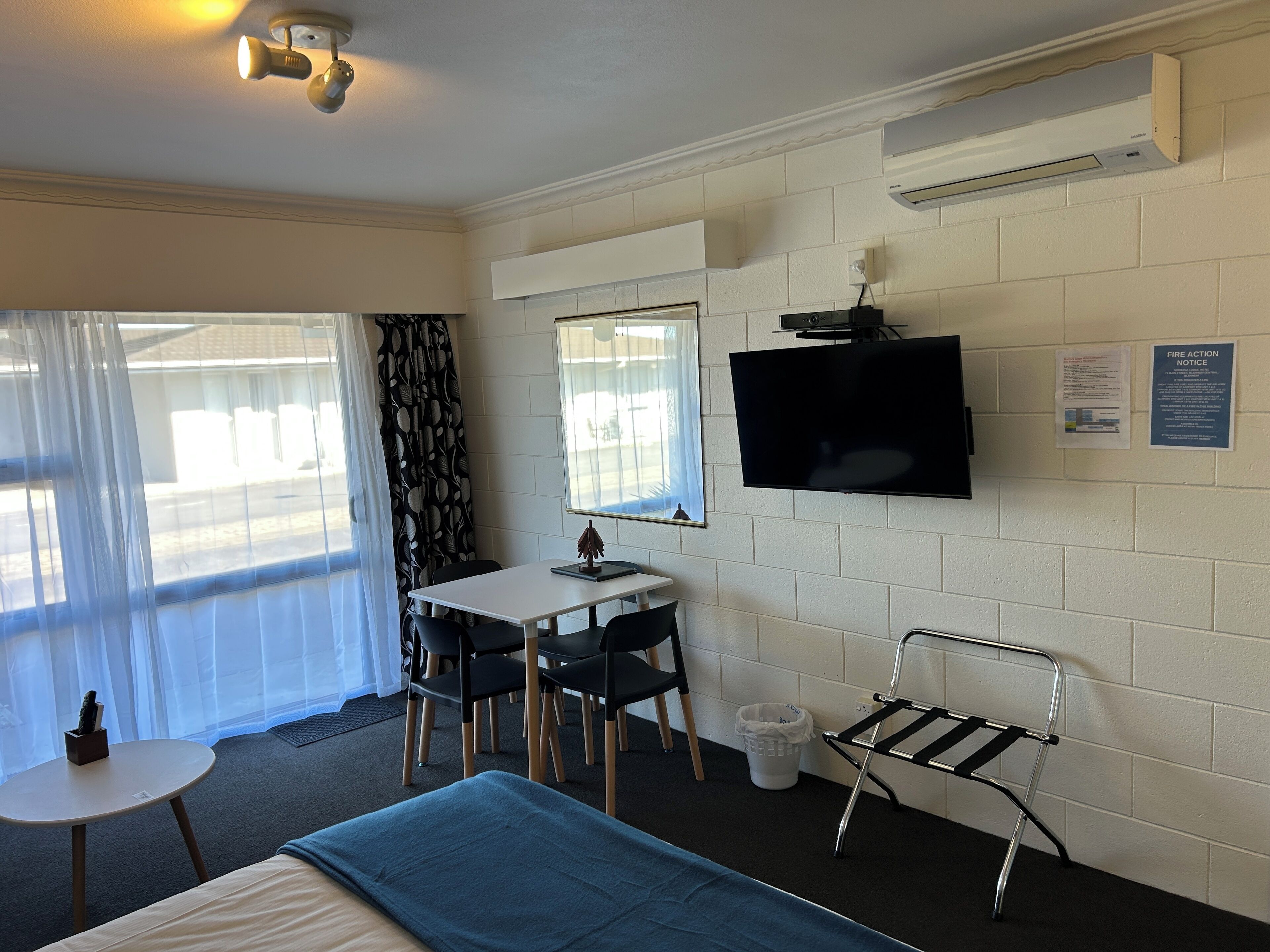 Habitación de hotel con cama, escritorio y sillas, televisor montado en la pared y ventana con cortinas.