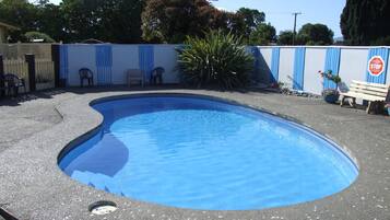 Una piscina con borde curvo, rodeada por una solana de concreto y una cerca azul.