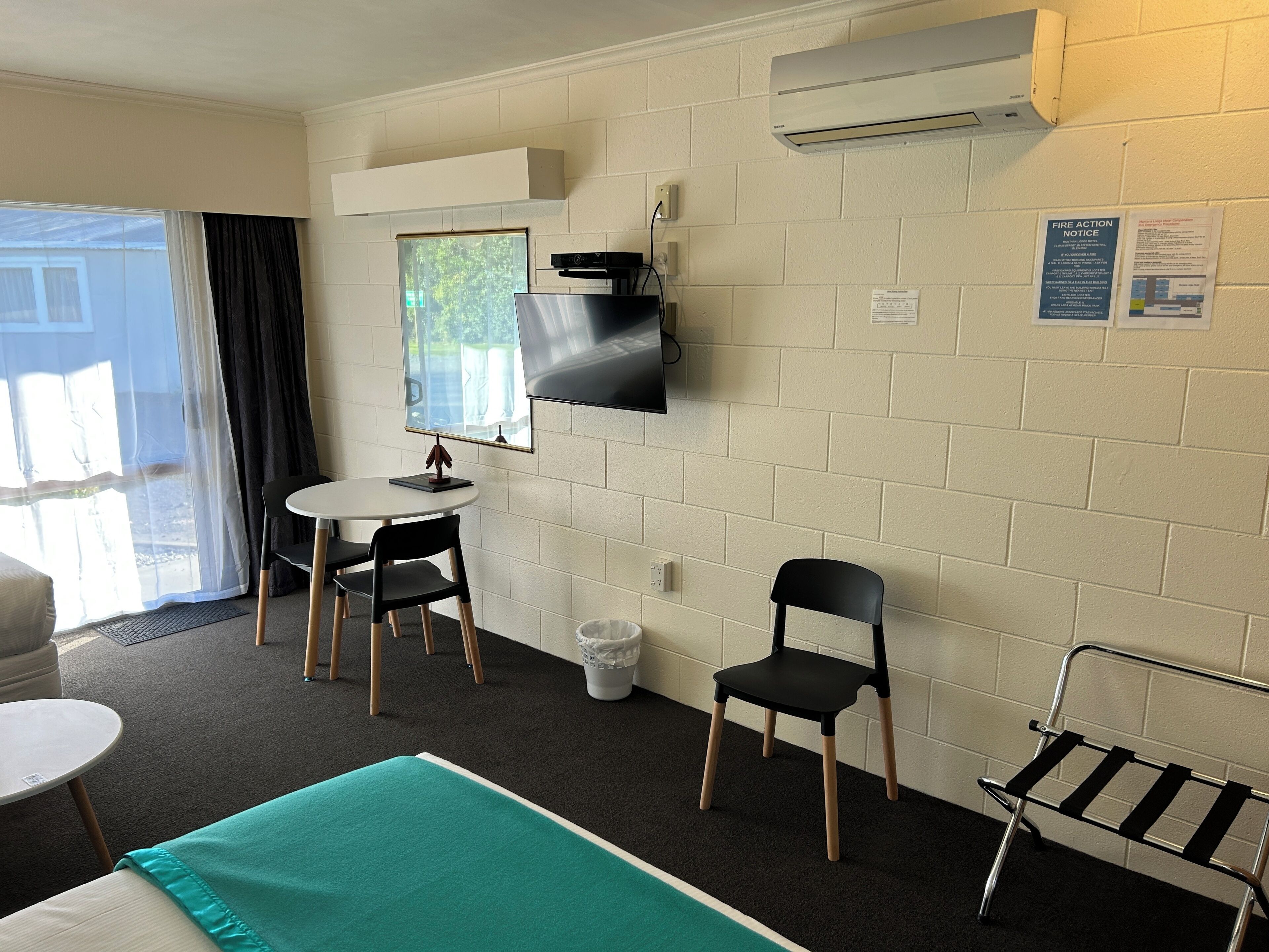 A room with a bed, a small table, two chairs, a TV, and an air conditioning unit.