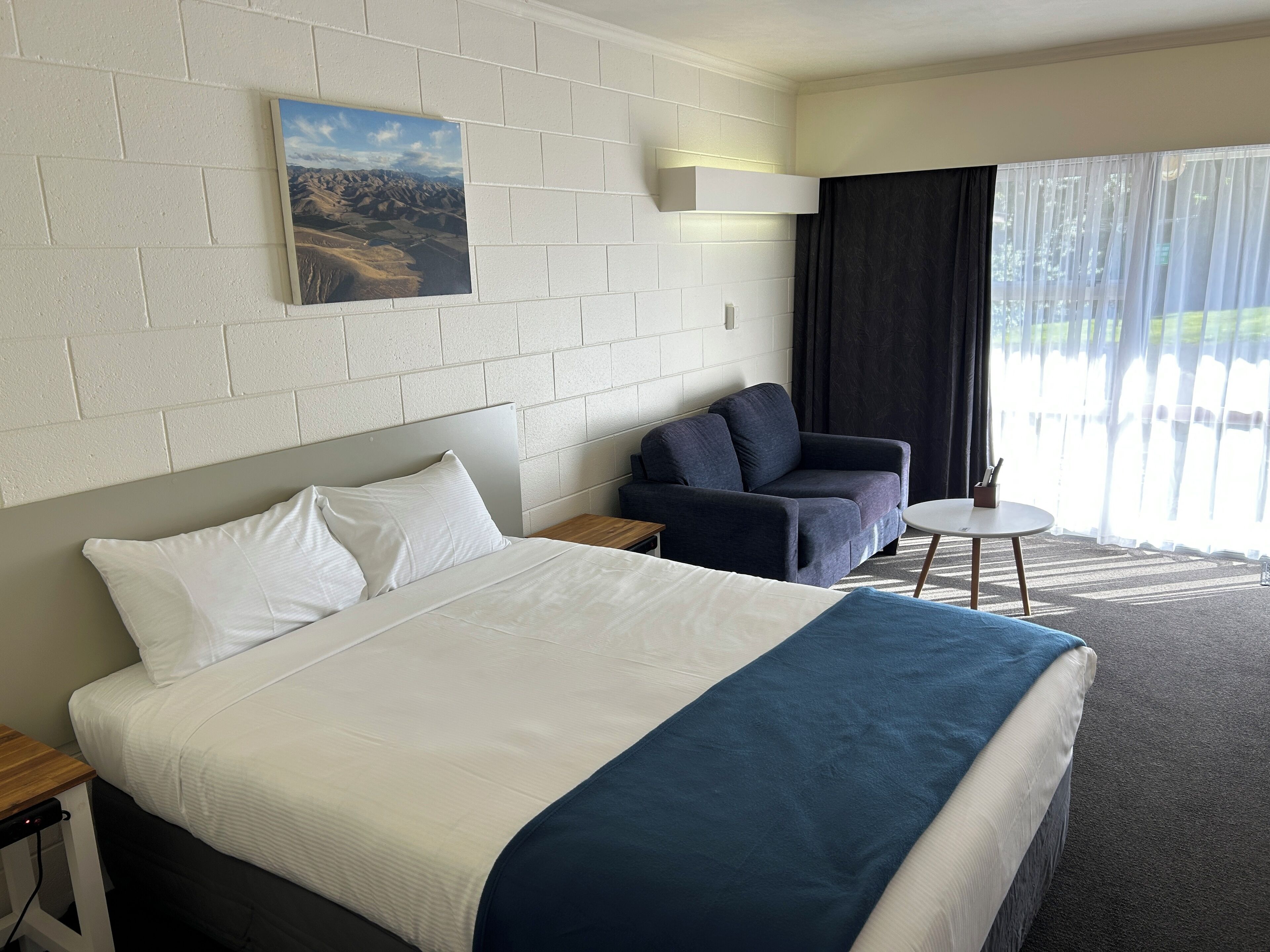 A hotel room with a large bed, a sofa, a small table, and a window with curtains.