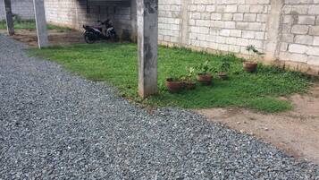 Un camino de grava que conduce a un área de estacionamiento techada, con un muro de concreto y plantas en macetas.