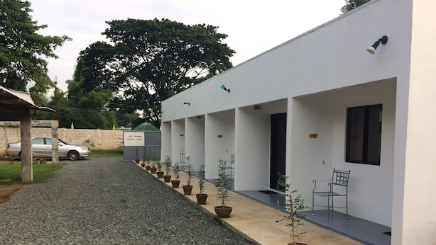 Un bâtiment avec un chemin de gravier menant à un espace abrité agrémenté de plantes en pot et de sièges.