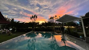 A swimming pool reflecting trees and a sunset sky.