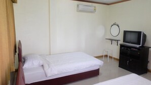 A hotel room with two beds, a TV, a small table, and an air conditioning unit.
