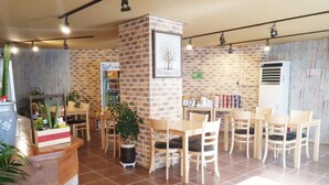 A cafe with brick walls, wooden tables, and chairs. There are potted plants and a self-service beverage station. - Happy Q Motel (Andong)
