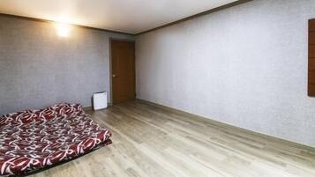 A bedroom with a bed, a wooden floor, a door, and a wall-mounted light fixture.