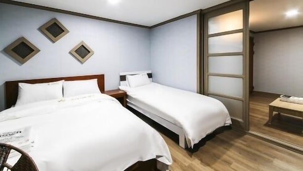 A hotel room with two beds, a wooden floor, and a sliding door leading to a bathroom. - Happy Q Motel (Andong)