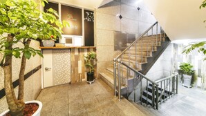 A modern hotel lobby with a staircase, potted plants, and a reception desk. - Happy Q Motel (Andong)