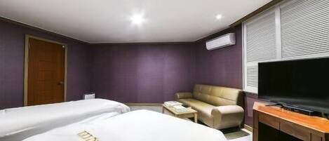 Een hotelkamer met twee eenpersoonsbedden, een slaapbank, een televisie en een airconditioning.