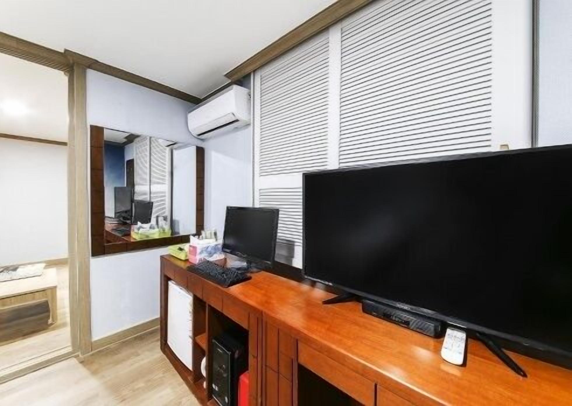 Et hotelværelse med skrivebord i træ, et fladskærms-tv, et spejl og et vindue med skodder.