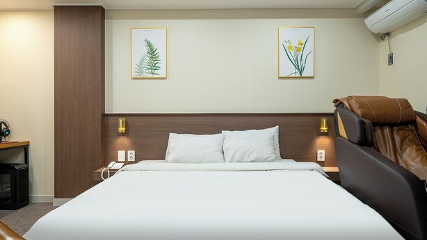 A hotel room with a large bed, two wall-mounted lamps, and two framed botanical prints. - Hotel Yaja Jecheon Station (Jecheon)