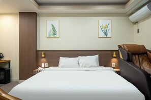 Habitación de hotel con una cama grande, dos lámparas fijadas a la pared y dos láminas enmarcadas con motivos botánicos.
