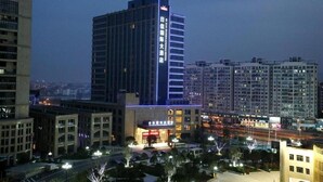 A high-rise hotel with a prominent sign, surrounded by other buildings and a well-lit street. - New Century Hotel Yiwu (Jinhua)