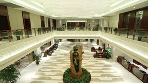 A spacious hotel lobby with a central decorative tree sculpture, multiple seating areas, and a high ceiling with intricate lighting. - New Century Hotel Yiwu (Jinhua)