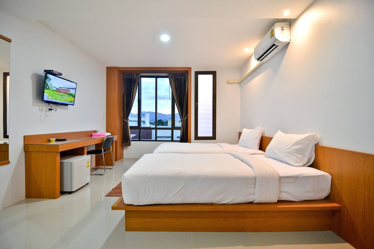 Habitación de hotel con cama, escritorio, silla, televisor, aire acondicionado y ventana con cortinas.