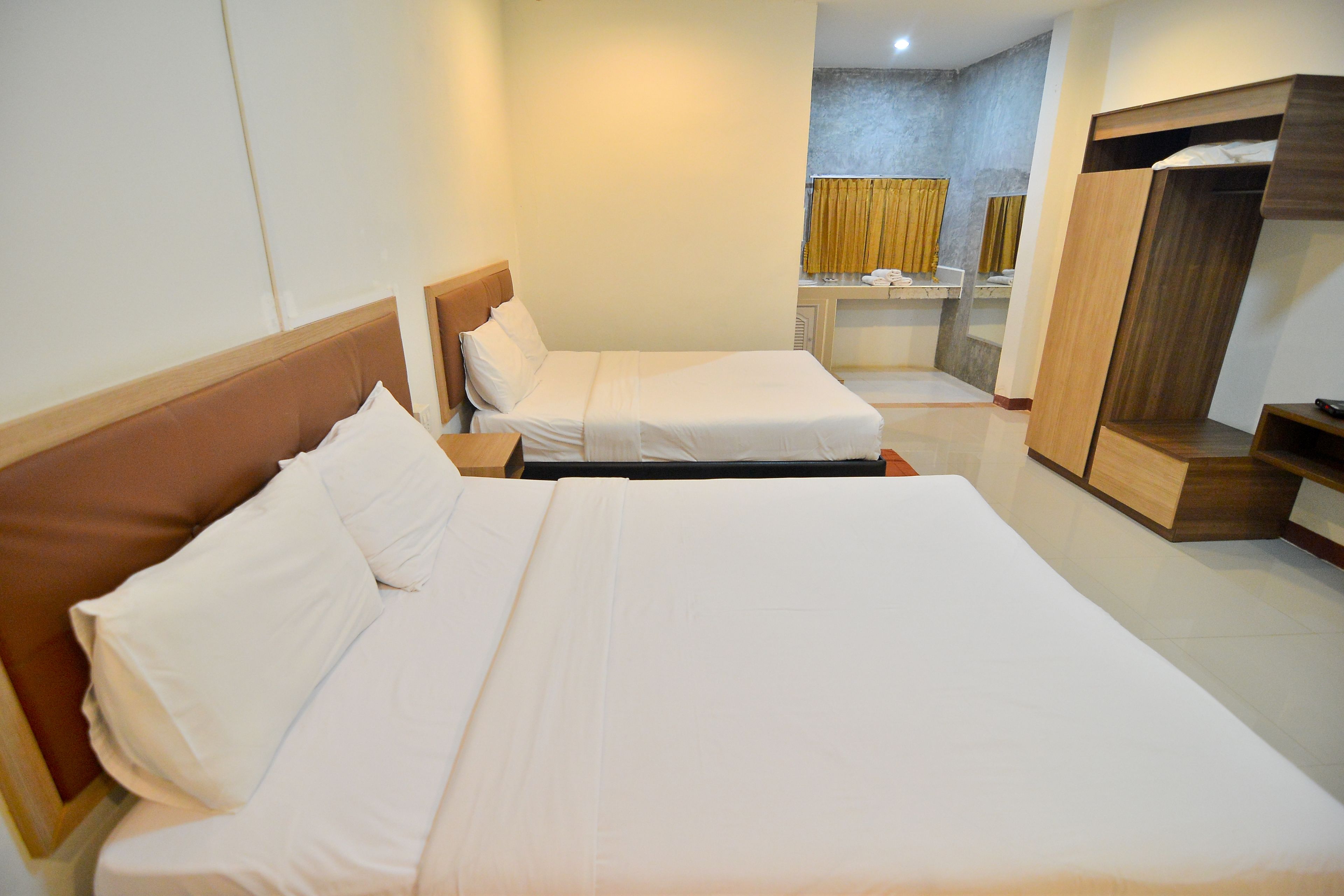 Une chambre d’hôtel avec deux lits, une armoire en bois et une petite salle de bain équipée d’un miroir et d’un porte-serviettes.