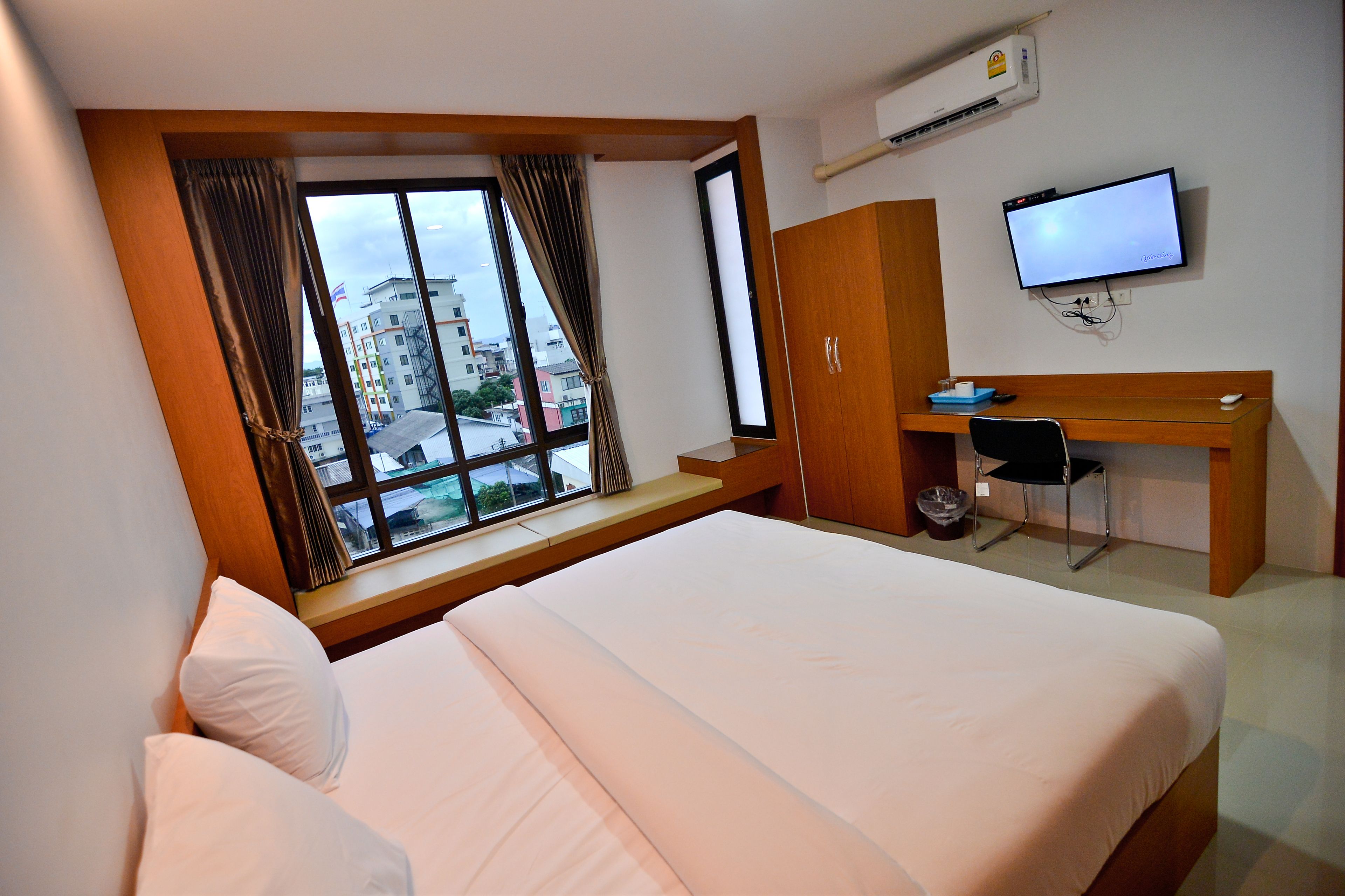 A hotel room with a large bed, a desk with a computer, and a window with curtains.