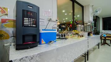 Una máquina expendedora, una cafetera y una mesa de buffet con comida y bebidas.