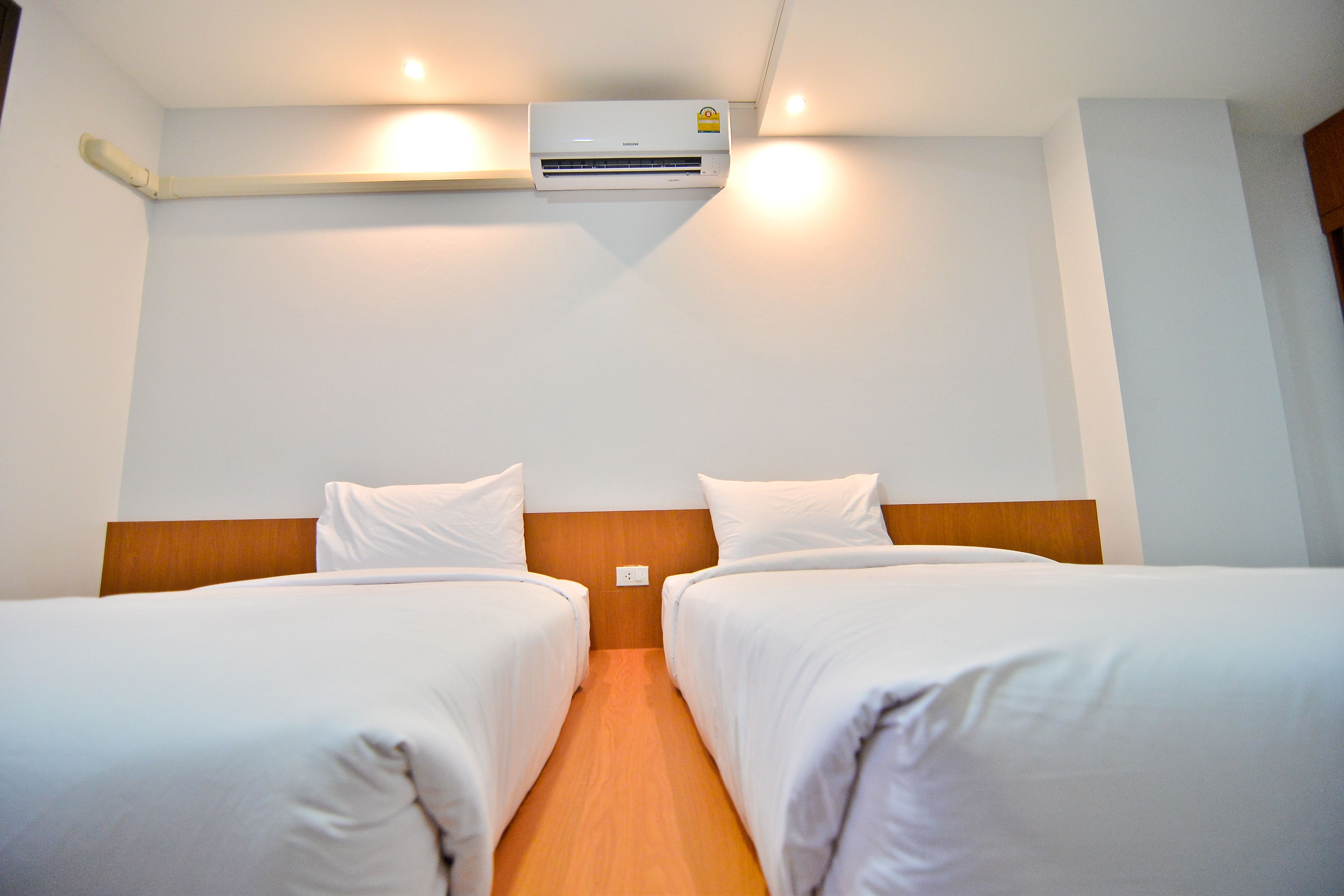 Habitación de hotel con dos camas individuales, cabecero de madera, ropa de cama blanca y un equipo de aire acondicionado montado en la pared.