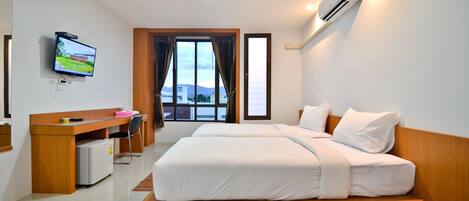 A hotel room with a bed, desk, chair, TV, and an air conditioner.