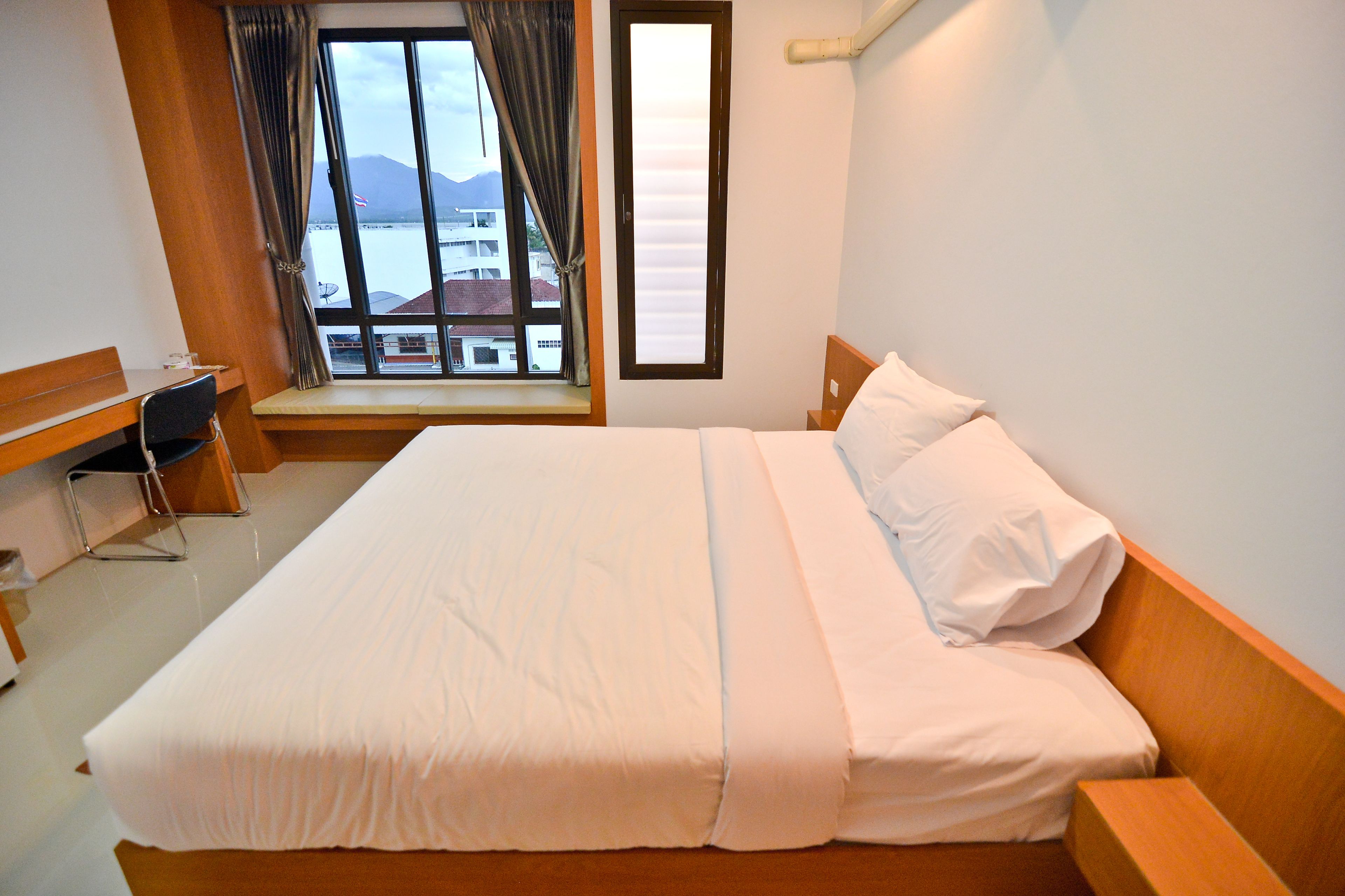 A neatly made bed with white linens, a wooden headboard, and a window with curtains.