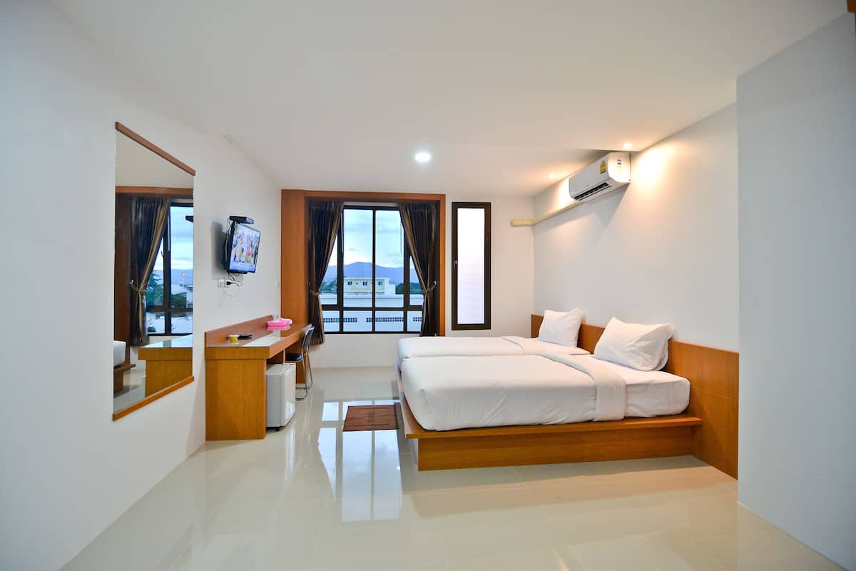 Habitación de hotel con cama, escritorio, silla, televisor y ventana con cortinas.