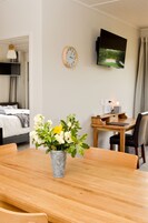 Habitación de hotel con mesa de comedor de madera, un jarrón con flores, un reloj, un televisor de pantalla plana y una cama con vista a un campo de golf.