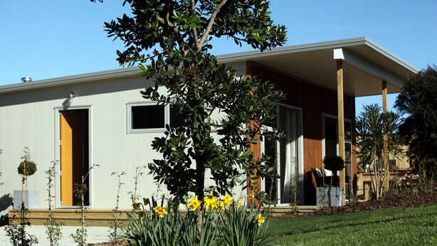 A modern house with a covered porch, a small garden with yellow flowers, and a clear blue sky.