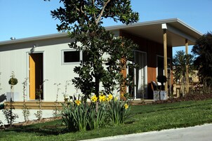 Una casa moderna con un porche cubierto, un pequeño jardín con flores amarillas y un cielo azul despejado.