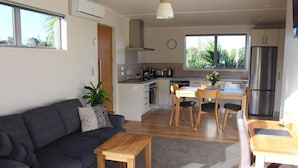 A modern living room with a sofa, coffee table, and dining area with chairs. There is a kitchen with a refrigerator, stove, and sink.