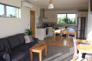 Una sala moderna con sofá, mesa de centro y comedor con sillas. Hay una cocina con refrigerador, estufa y pileta.