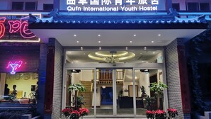 Het uiterlijk van Qfun International Youth Hostel, met een traditionele Chinese architectuur, inclusief een neonbord, bloempotten en een moderne entree.