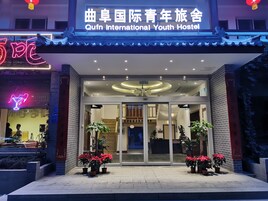 The exterior of Qfun International Youth Hostel with a traditional Chinese architectural style, featuring a neon sign, potted plants, and a modern entrance.