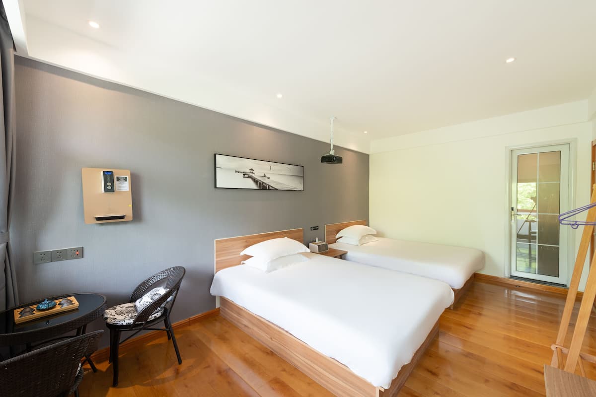 Hotelkamer met houten vloer, een bed met witte lakens, een stoel, een tafel, een wandheater en een raam met uitzicht.